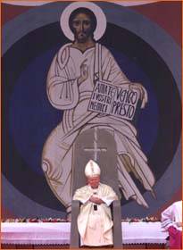 [Bild: Der Papst auf seinem Thron mit dem umgedrehten Kreuz vor einem Bild von Jesus]